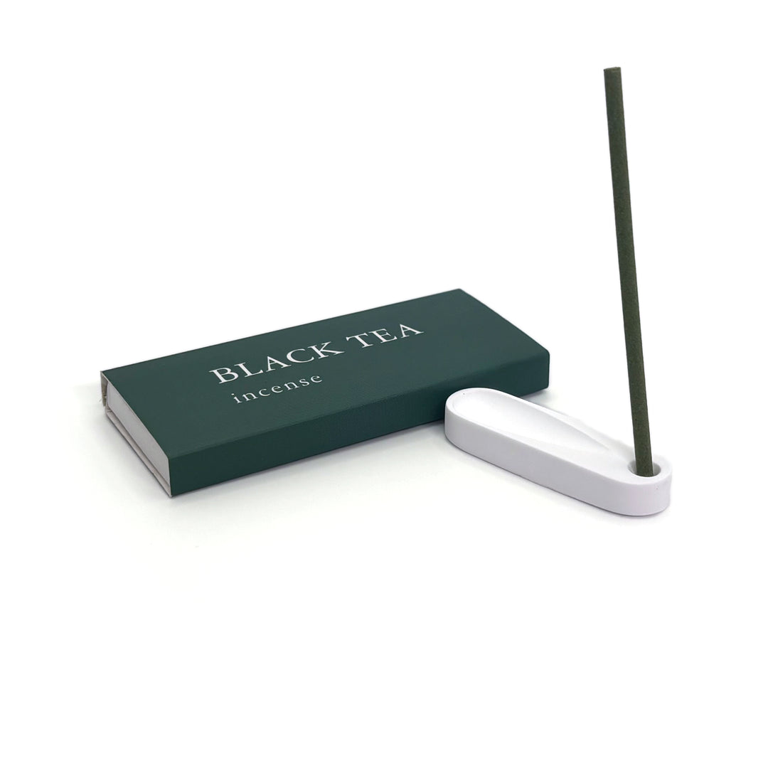Burning black tea incense stick placed in minimalist plaster holder next to green box