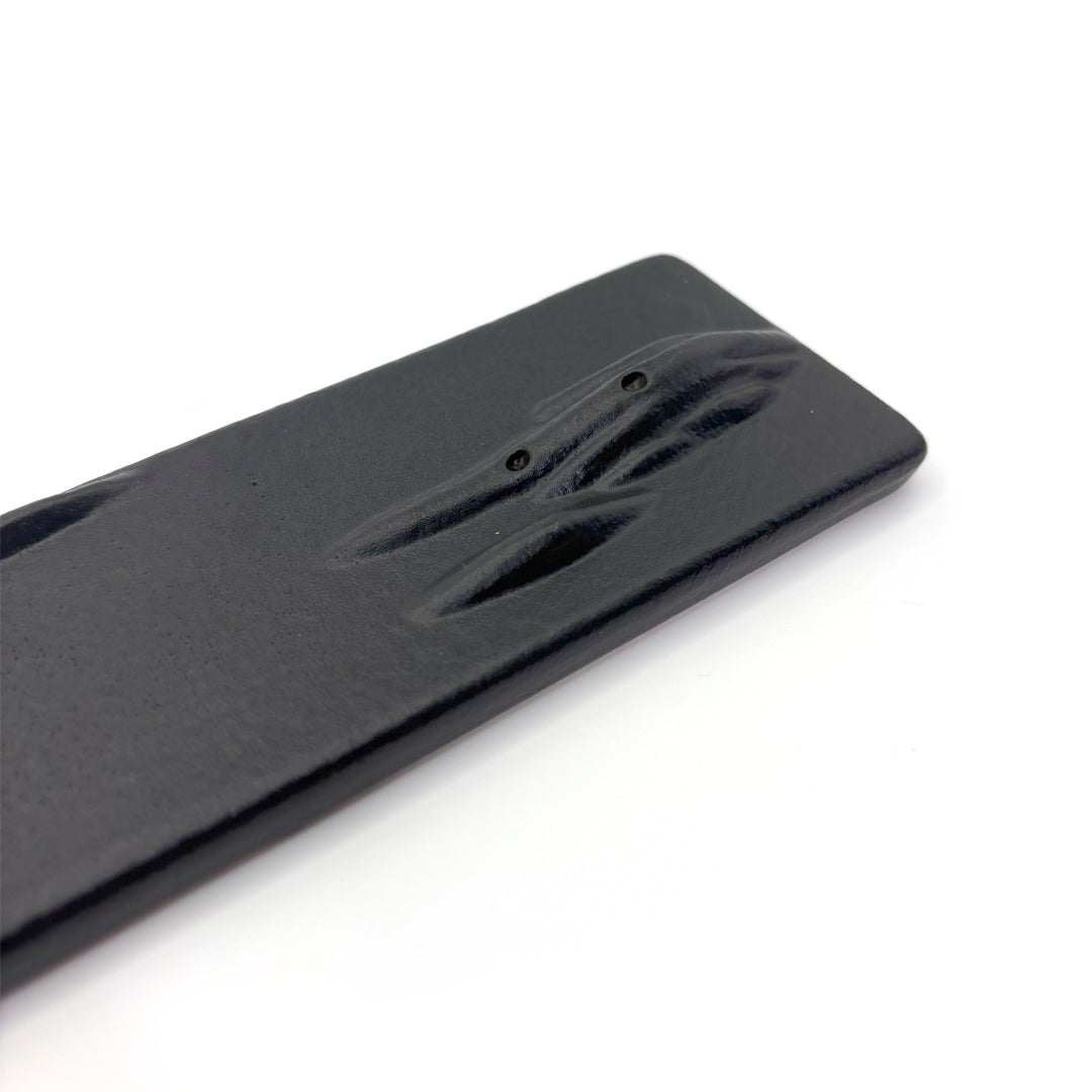 Close-up of dual incense holes on a black ceramic holder with oriental mountain texture