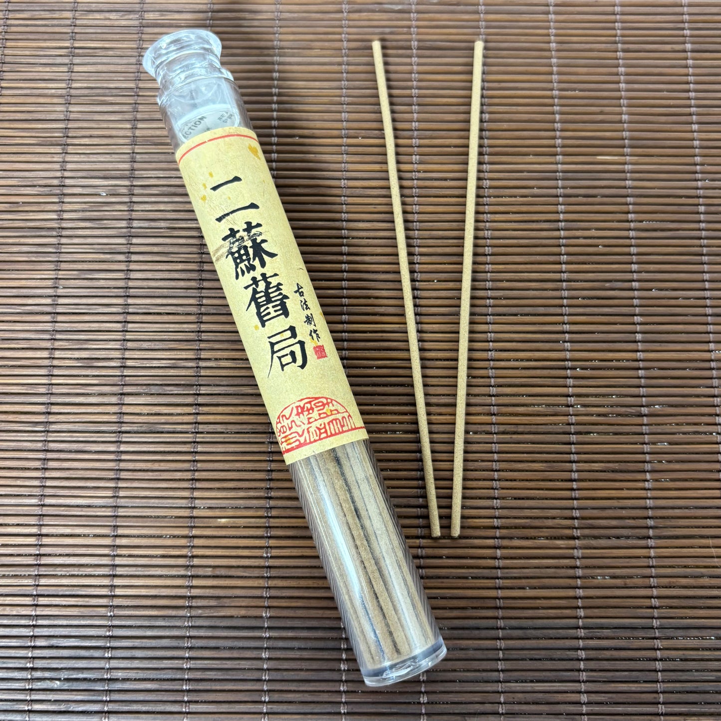 Er Su Old Studio incense in plastic tube with warm-toned short sticks on bamboo mat