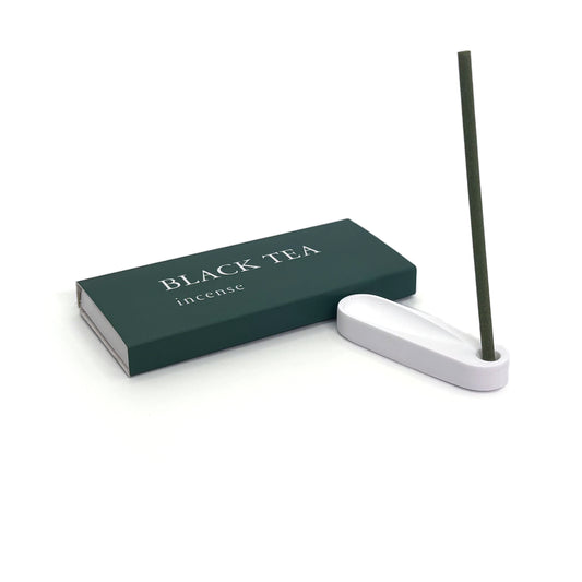 Burning black tea incense stick placed in minimalist plaster holder next to green box