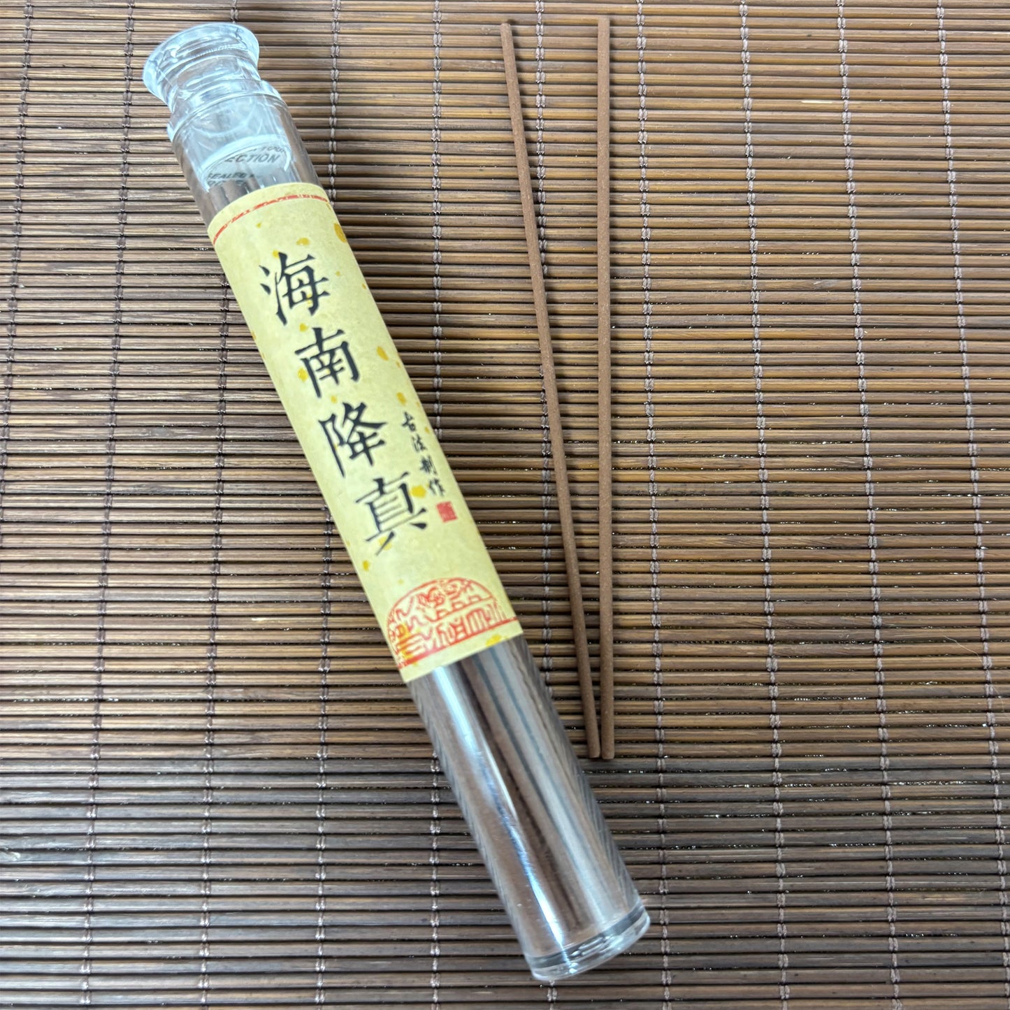 Hainan Aloeswood incense sticks in a clear plastic tube, laid out on a bamboo mat