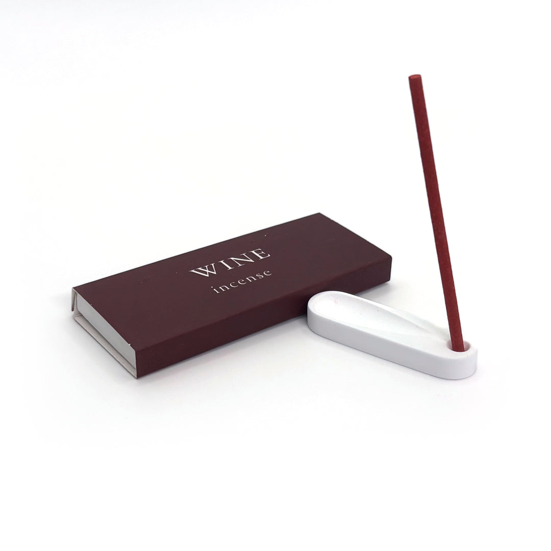Red wine incense burning in plaster holder, next to wine-themed packaging
